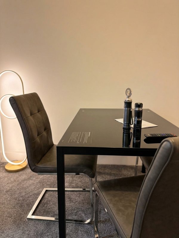 Modern workspace with black desk, two chairs, neon loop lamp, and desk accessories