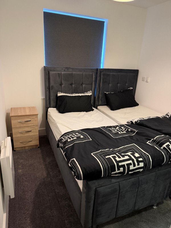 Modern bedroom with double bed, black headboard, geometric bedding, and wooden nightstand
