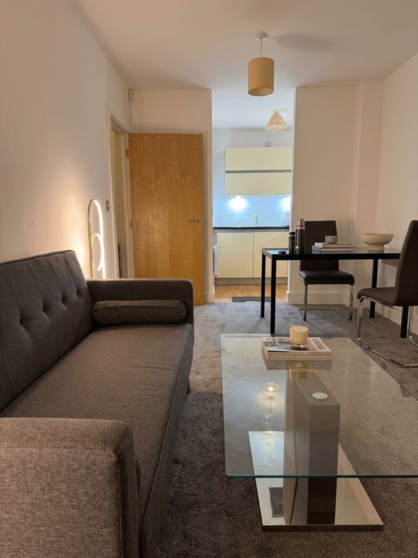 Open-plan living room with grey sofa, glass coffee table, black desk and chair, wooden door