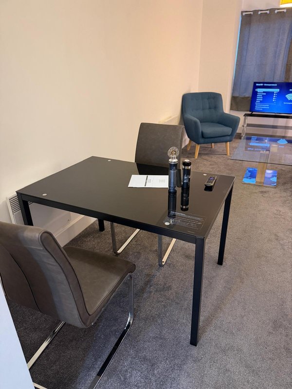 Modern workspace with black dining table, grey chairs, TV monitor, and armchair in bright room
