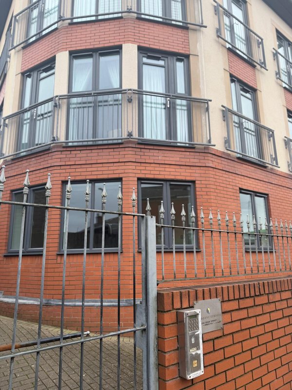 Red brick corner building exterior with curved balconies, metal railings and ground-floor entrance