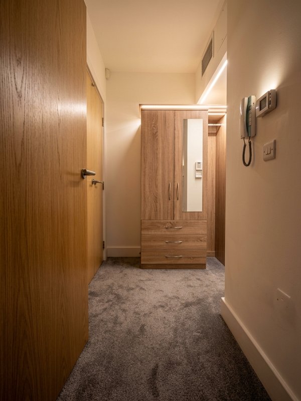 Hallway with wooden door, wardrobe, carpet flooring and wall-mounted telephone