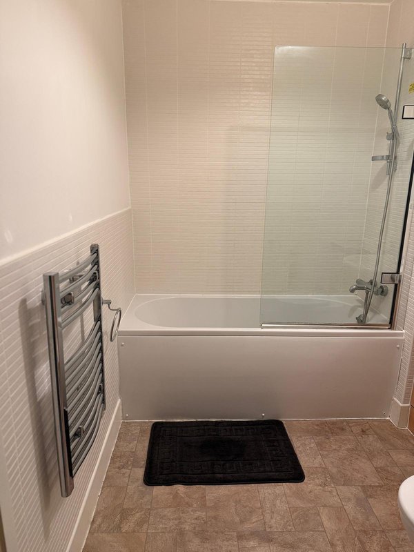 Modern bathroom with white subway tile walls, glass shower enclosure, heated towel rail and dark bath mat