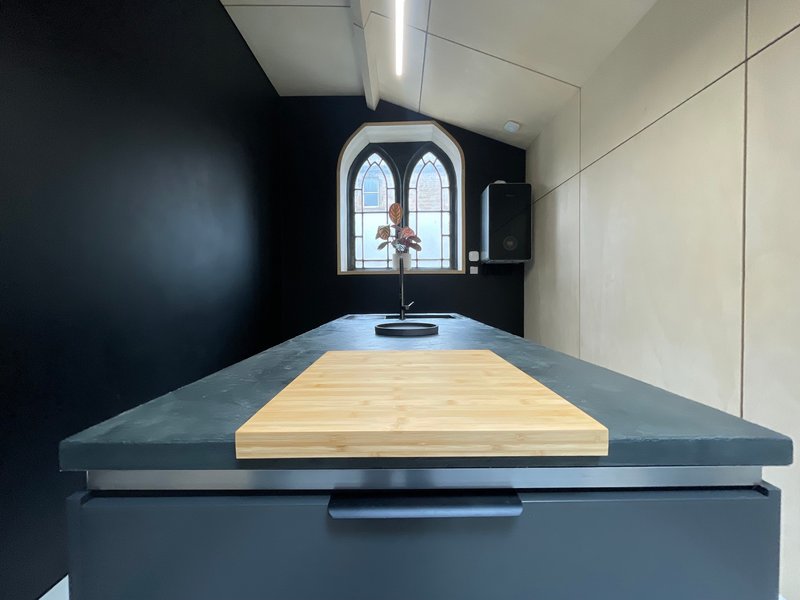 Modern kitchen with dark cabinetry, wooden countertop, arched window and minimalist design