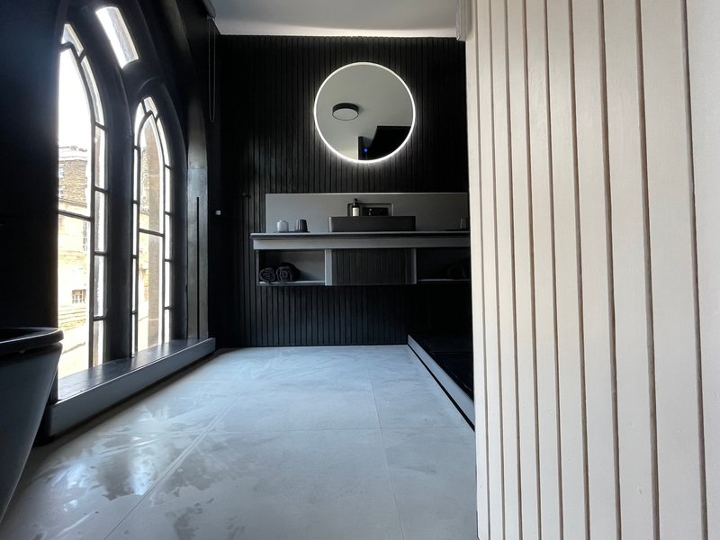 Modern bathroom with circular mirror, black wall paneling, large window and light blue floor