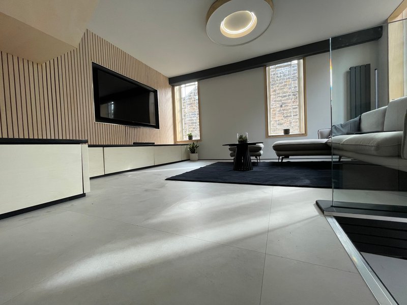 Modern open-plan living room with white flooring, wall-mounted TV, sofa, and natural lighting