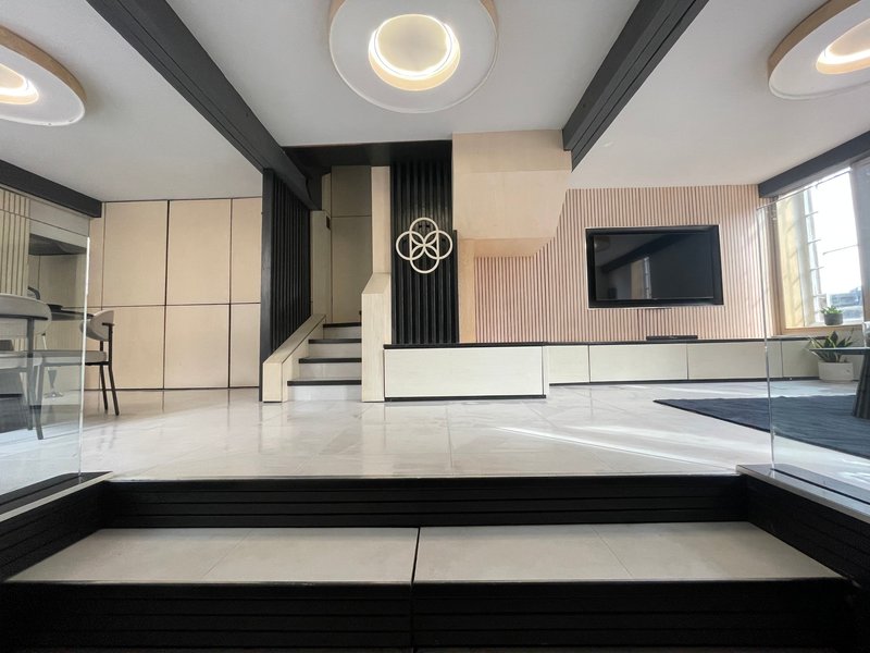 Modern open-plan living space with white cabinetry, black beams, staircase and recessed lighting