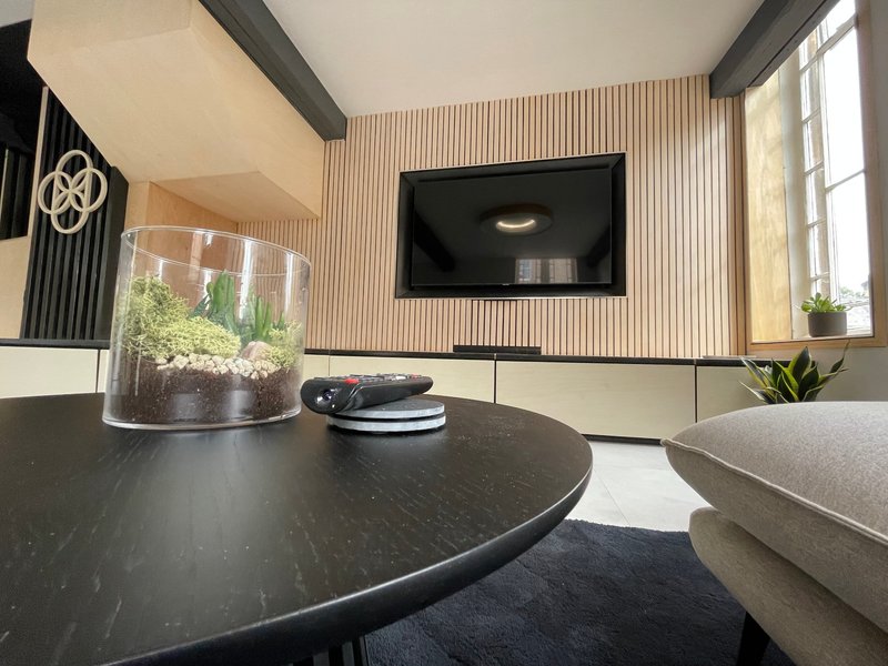 Modern living room with round black table, wall-mounted TV, decorative plant and seating area
