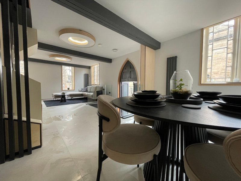 Modern open-plan dining and kitchen area with black table, beige chairs, and exposed beam ceiling