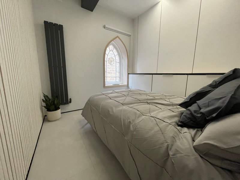 Modern bedroom with double bed, black pillows, radiator and arched window