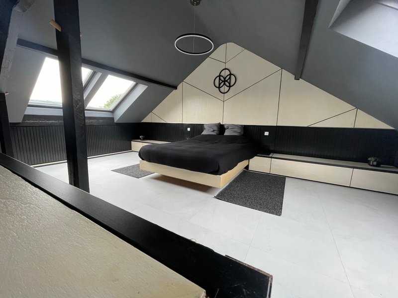 Modern loft bedroom with black platform bed, sloped ceiling, skylights and minimalist furnishings