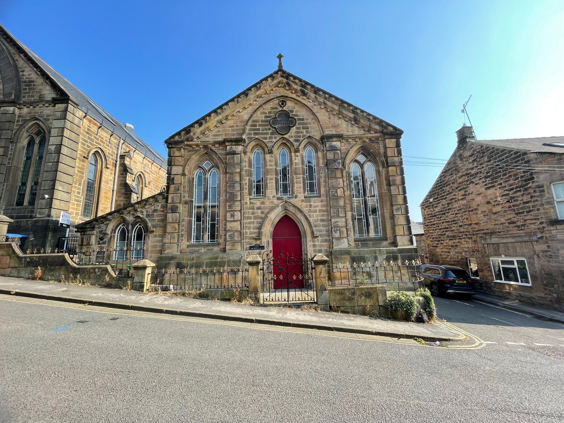 Stone chapel building with red door, arched windows and clear blue sky