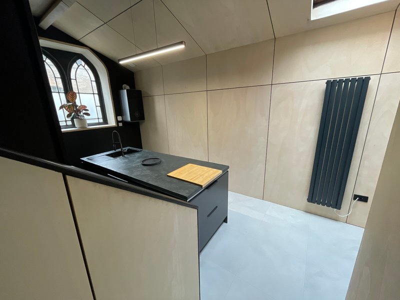 Modern bathroom with black vanity, pale tile walls, vertical radiator and arched window
