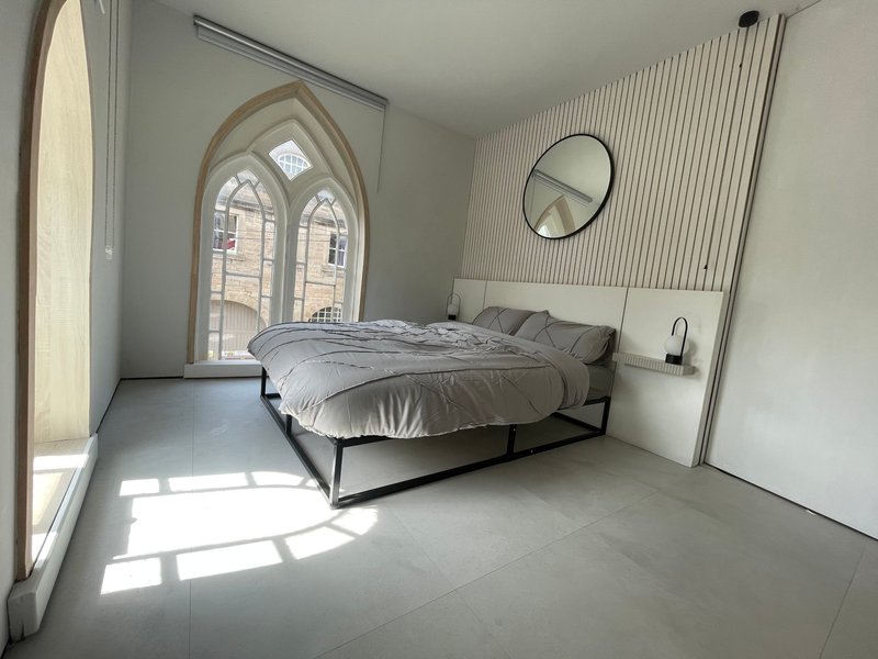 Modern bedroom with double bed, arched window, round mirror and minimalist décor