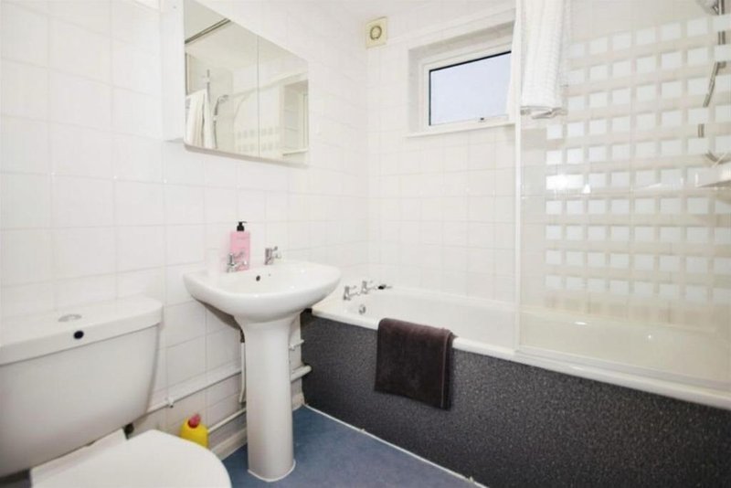 Clean bathroom with white tile walls, pedestal sink, toilet, bathtub and shower enclosure