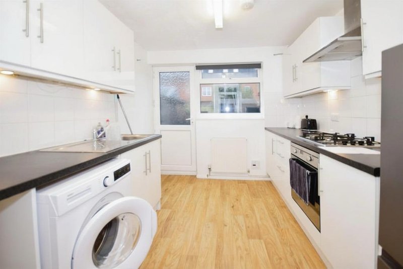 Modern kitchen with white cabinetry, black countertops, integrated appliances and wooden flooring
