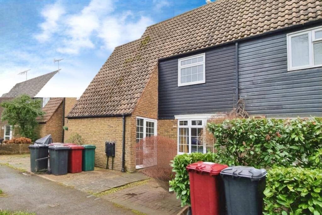 Exterior of brick cottage with tiled roof, driveway, colorful bins and hedges