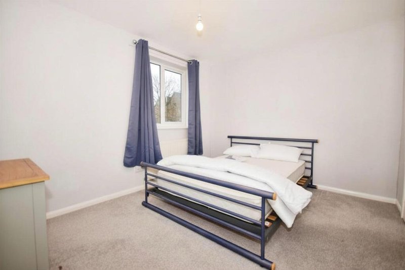 Bedroom with metal-frame bed, blue curtains, white bedding, and small wooden side table