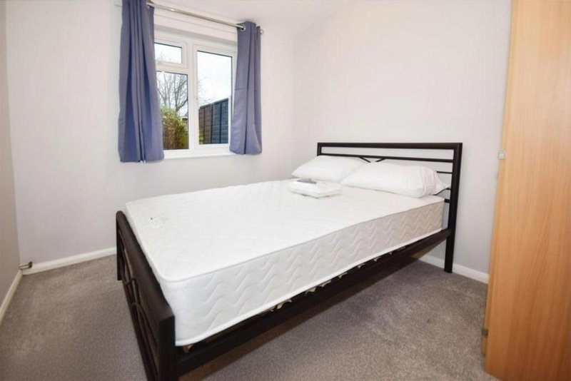 Bedroom with double bed, black metal frame, white bedding, window with blue curtains