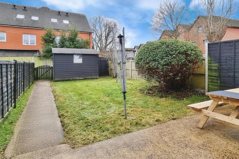 Rear garden with lawn, paved pathways, fencing, and neighboring brick houses visible