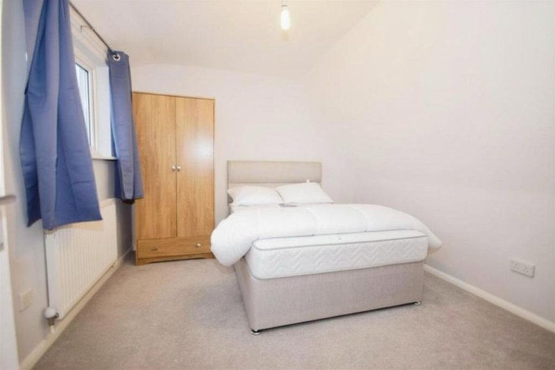 Bedroom with double bed, wooden wardrobe, blue curtains and beige carpet