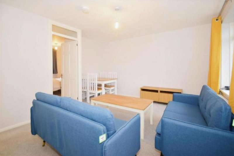 Bright open-plan living area with blue sofas, wooden table, and yellow curtains
