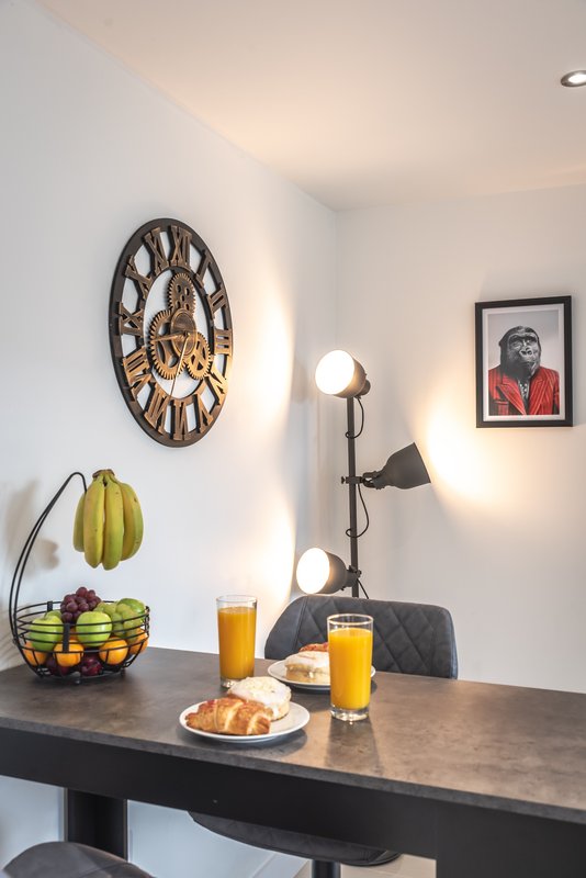 Modern dining area with dark table, breakfast spread, wall clock, and framed portrait
