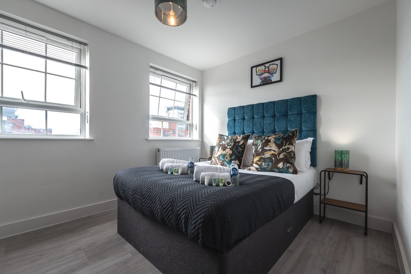 Bright bedroom with double bed, teal headboard, two windows and wooden flooring