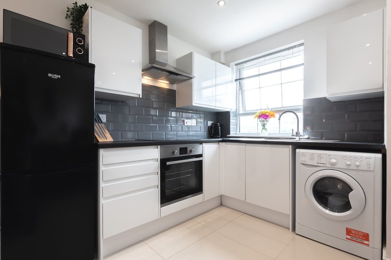 Modern kitchen with white cabinets, dark tile backsplash, black appliances and washing machine