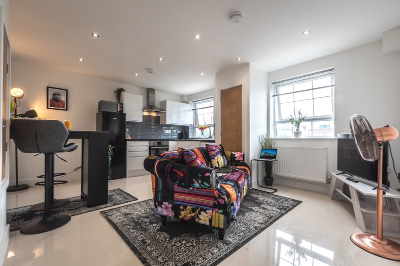 Modern open-plan living space with kitchen, colorful patterned armchair, and various furnishings