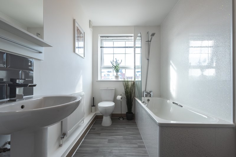 Modern bathroom with pedestal sink, toilet, bathtub and window with natural light