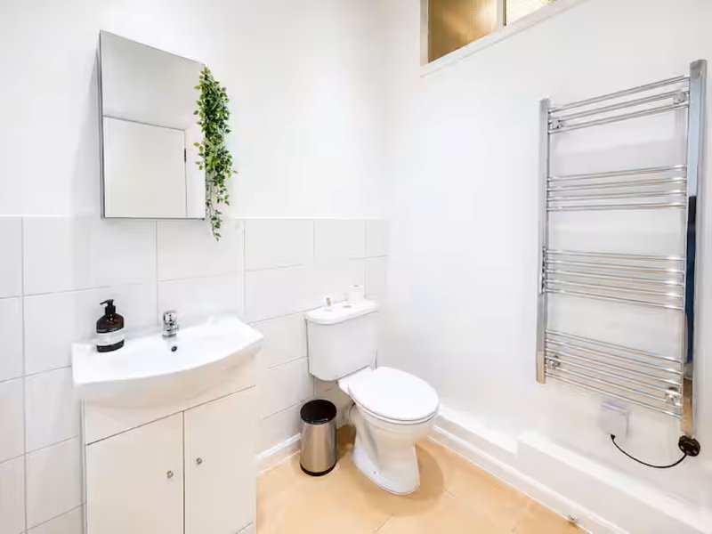 Clean modern bathroom with white tiles, sink, toilet, towel rail and mirror