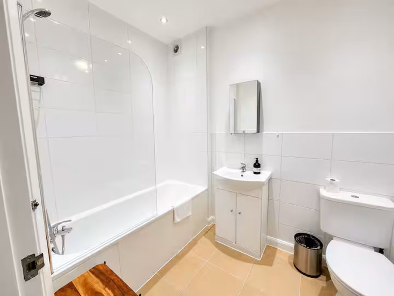 Modern bathroom with walk-in shower, white vanity, toilet, and wooden flooring