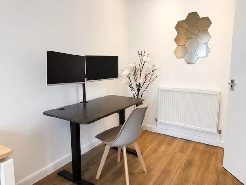 Modern home office with dual monitors, black desk, grey chair and wooden flooring