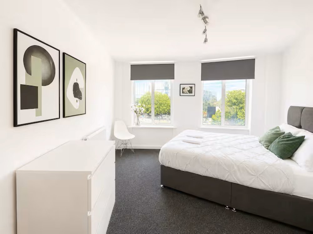 Bright modern bedroom with double bed, framed wall art, windows with grey blinds and garden views