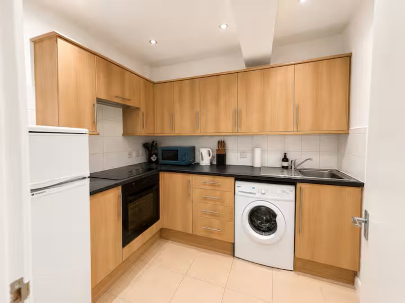 Modern kitchen with wooden cabinets, black countertops, built-in oven and washing machine