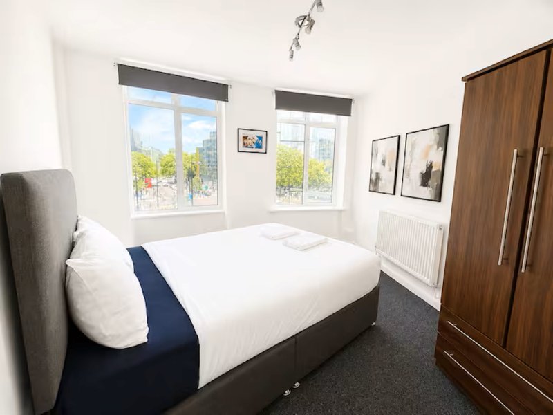 Bright modern bedroom with double bed, wooden wardrobe, and large windows overlooking garden