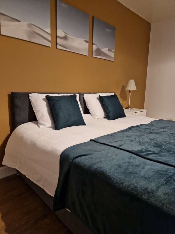 Modern bedroom with double bed, teal bedding, decorative pillows and wall art