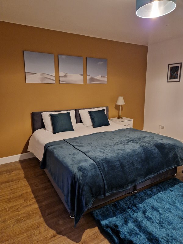 Modern bedroom with double bed, dark blue bedding, cushions, wooden floor and ochre accent wall