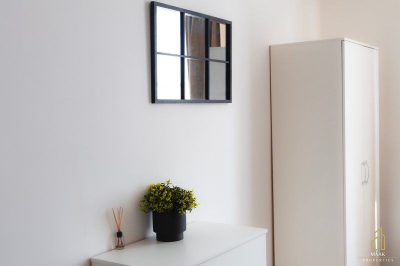 Minimalist bedroom corner with white dresser, potted plant, mirror and wardrobe