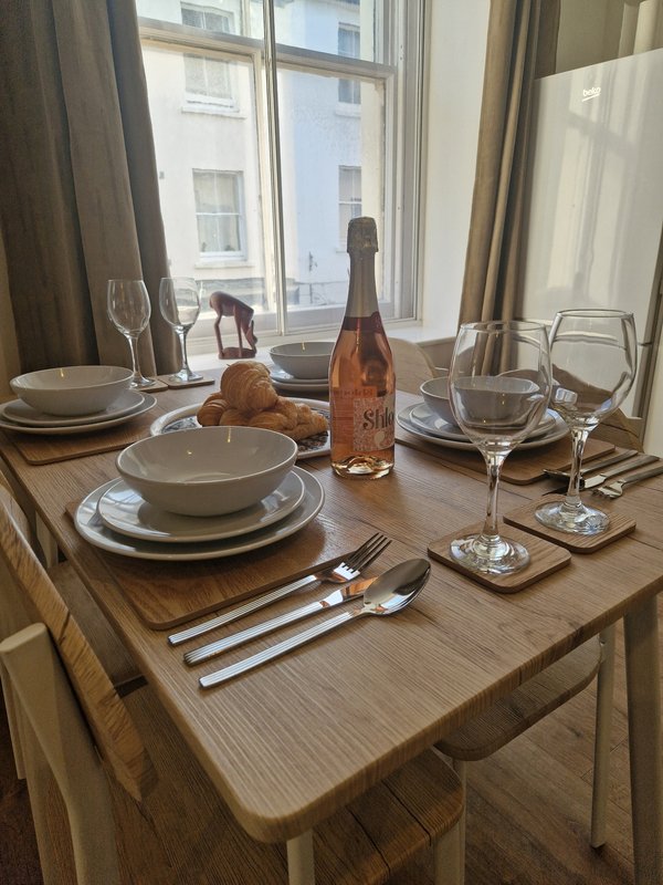Dining table set for two with wine bottle, glasses, plates and cutlery by window