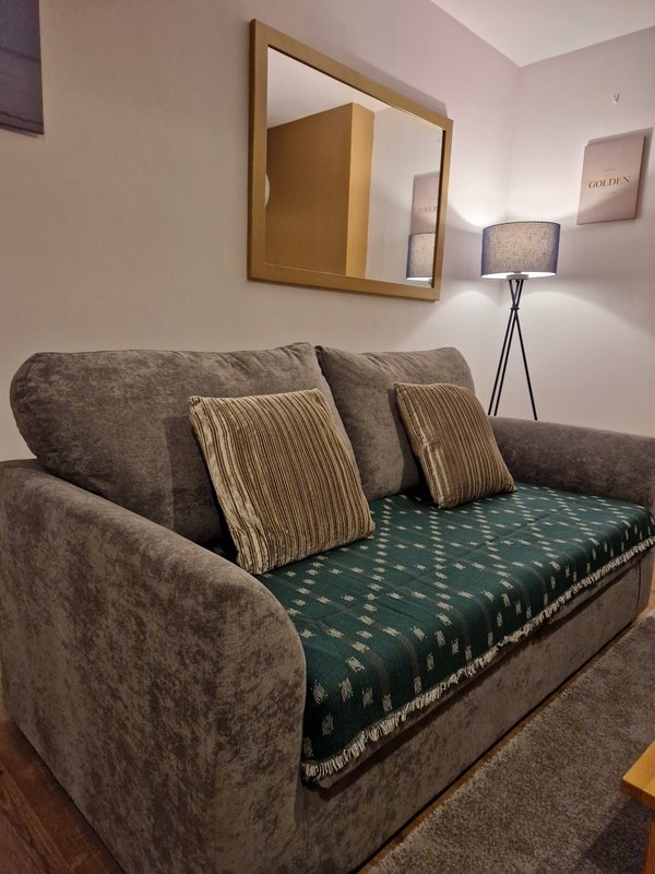 Living room with gray upholstered sofa, striped and patterned cushions, wooden-framed mirror, and tripod floor lamp