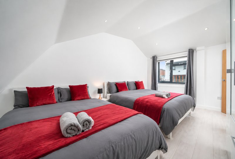 Modern bedroom with two double beds, red and grey bedding, white walls and wooden flooring