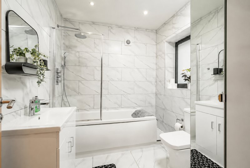 Modern bathroom with white marble tiles, glass shower enclosure, vanity sink and toilet