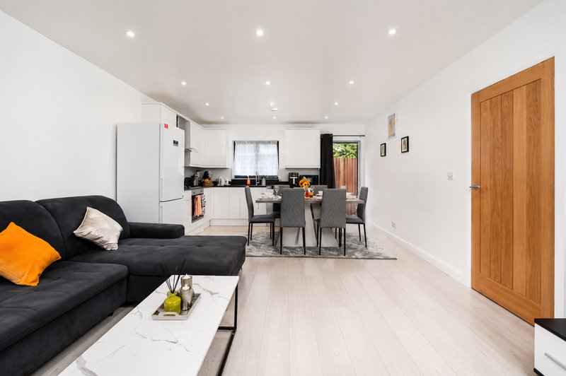Open-plan living room with black sofa, dining area, kitchen, and wooden door