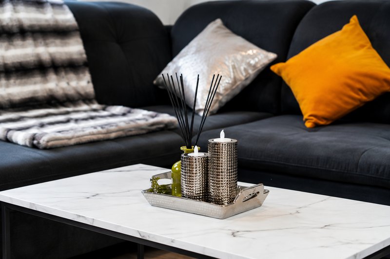 Modern living room with black sofa, marble coffee table, decorative cushions and table accessories
