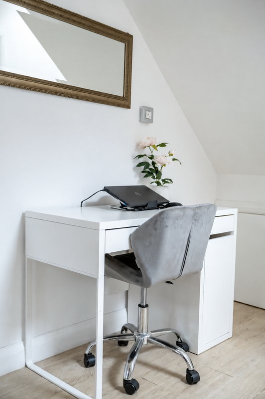 Minimalist home office with white desk, grey chair, potted plant and framed mirror
