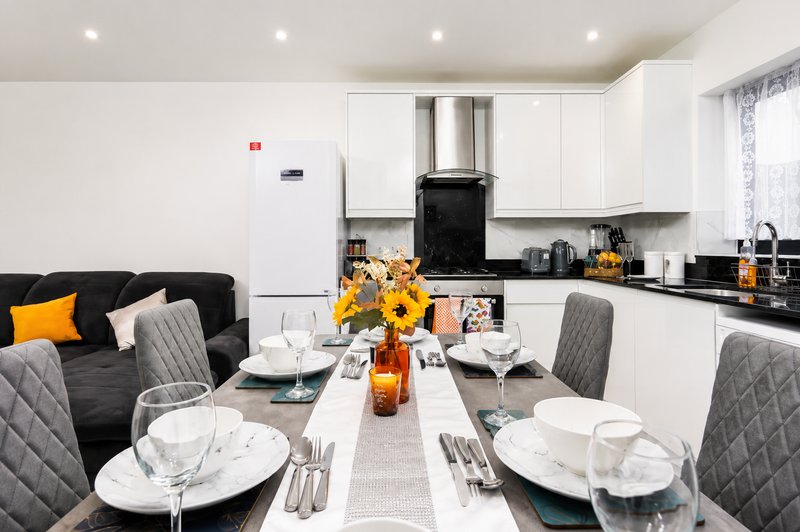 Open-plan kitchen and dining area with white cabinetry, black countertops, dining table set for four, and yellow flowers