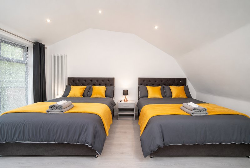 Twin bedroom with two double beds, yellow and grey bedding, arched ceiling, and contemporary lighting