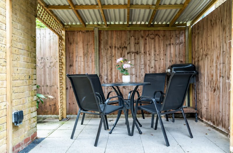 Covered patio area with dining table, black chairs, and potted flowers